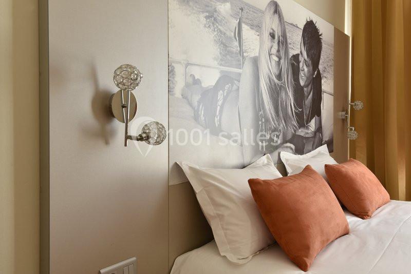 Tête de lit avec une photo en noir et blanc, lit double avec coussins orange et appliques murales modernes.