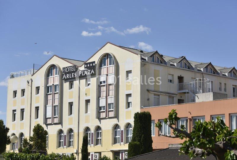 Façade d'un hôtel avec des fenêtres en arc, un panneau ’Hôtel Arles Plaza’ et un ciel bleu en arrière-plan.