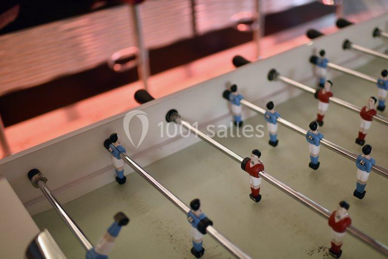 Vue rapprochée d'un baby-foot avec des figurines en tenue bleue et rouge sur un terrain clair.
