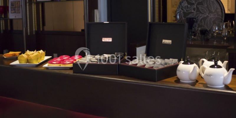 Buffet avec muffins, donuts, boîtes de sachets de thé et théières blanches sur un comptoir en bois.