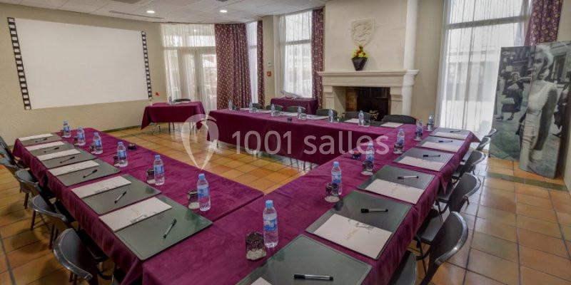 Salle de réunion aménagée en U avec tables violettes, blocs-notes, stylos et bouteilles d'eau, éclairée par la lumière…