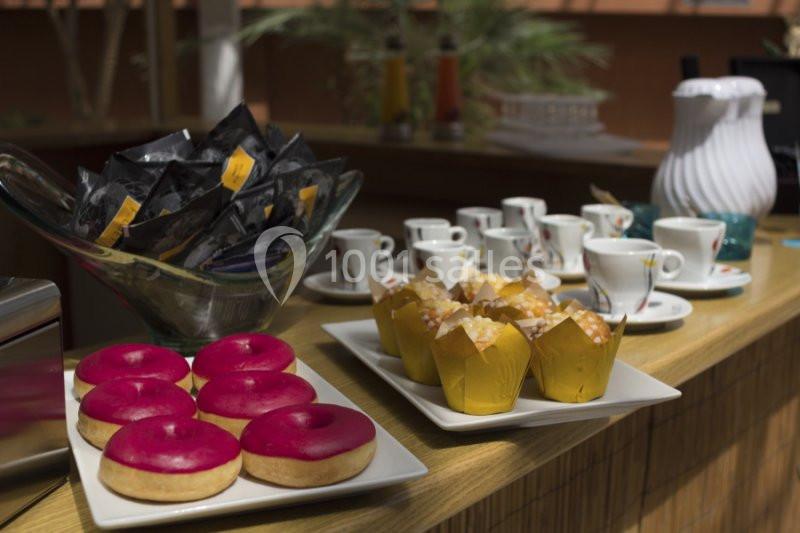 Assortiment de donuts, muffins, sachets de thé et tasses à café sur un comptoir en bois.