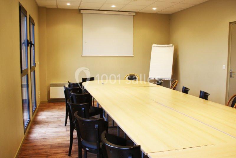 Salle de réunion avec une grande table en bois, des chaises noires, un paperboard et un écran de projection.