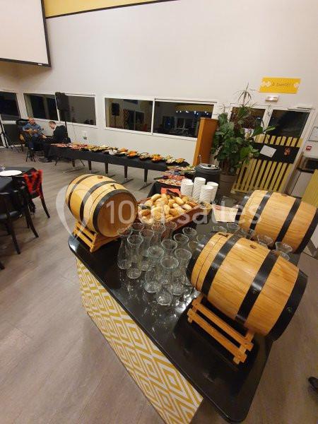 Buffet avec tonneaux décoratifs, verres, pains et plats variés dans une salle lumineuse avec grandes fenêtres.
