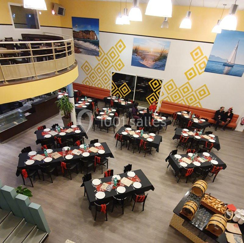 Salle de restaurant spacieuse vue de dessus, tables dressées avec nappes noires et décorations murales colorées.