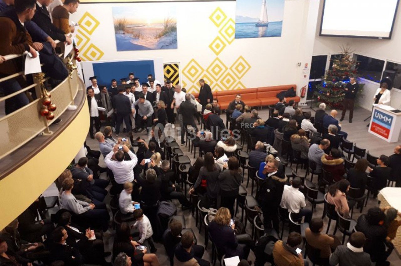 Salle comble avec des personnes assises et debout, assistant à une présentation près d'un écran et d'un sapin décoré.