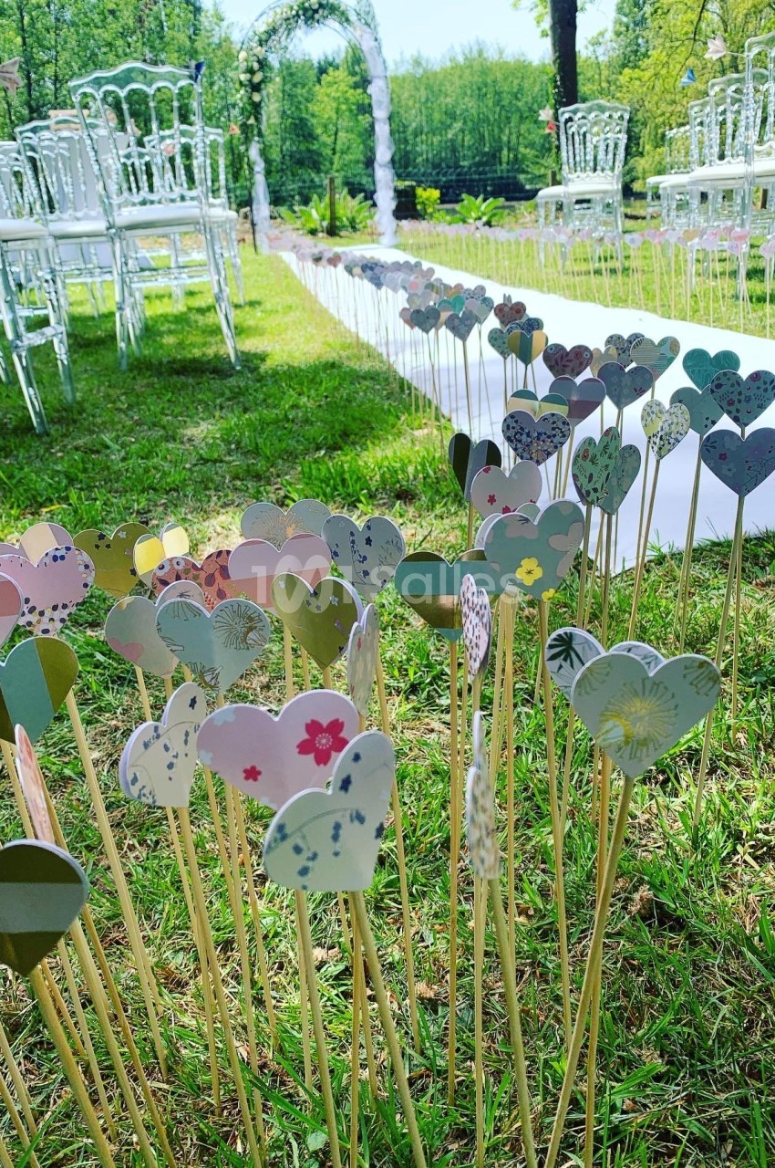 Cœurs en papier colorés plantés sur des tiges dans l'herbe, décorant une allée pour une cérémonie en plein air.