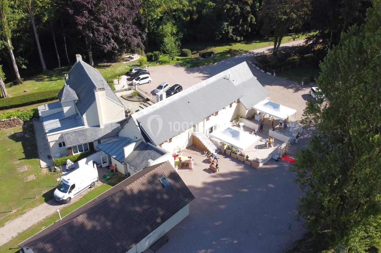Vue aérienne d'un bâtiment rural avec des toits en ardoise, entouré de verdure et de véhicules stationnés.