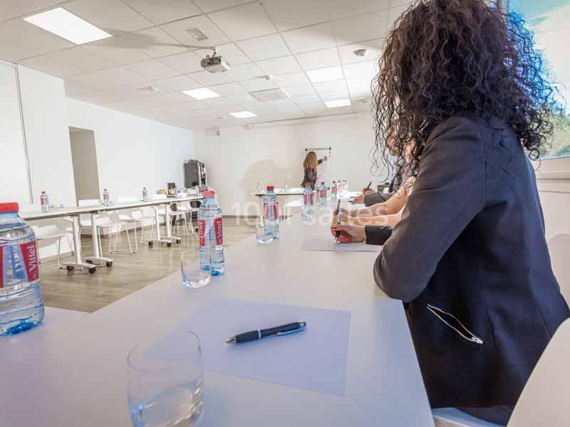 Une formatrice écrit sur un tableau blanc devant des participants assis dans une salle de réunion lumineuse.