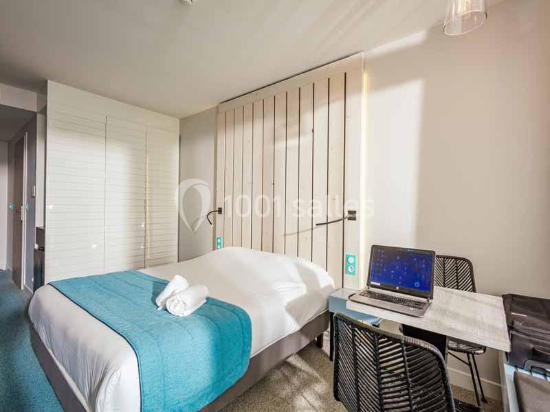 Chambre lumineuse avec lit double, bureau équipé d'un ordinateur portable et porte coulissante en bois clair.