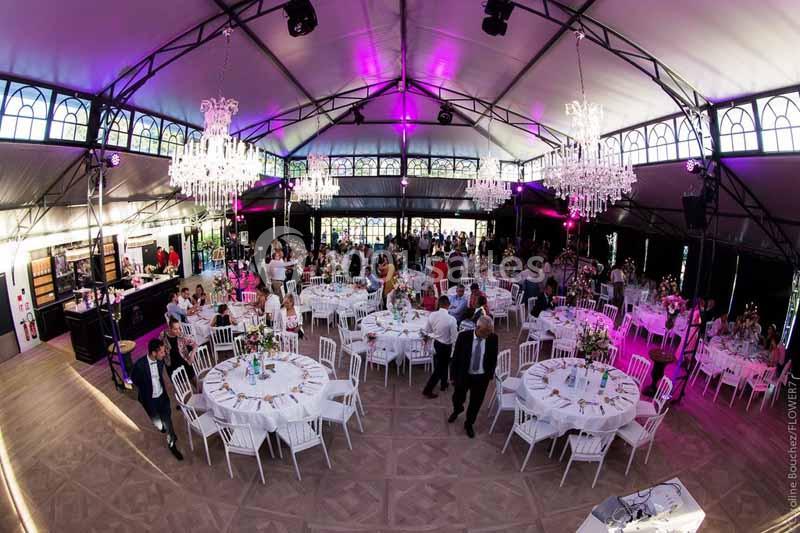 Salle de réception décorée avec des tables rondes, des chaises blanches et des lustres, accueillant des invités.