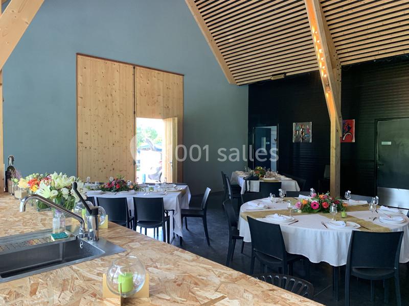 Salle de réception moderne avec tables rondes dressées, décorée de fleurs colorées et éclairée par la lumière naturelle.