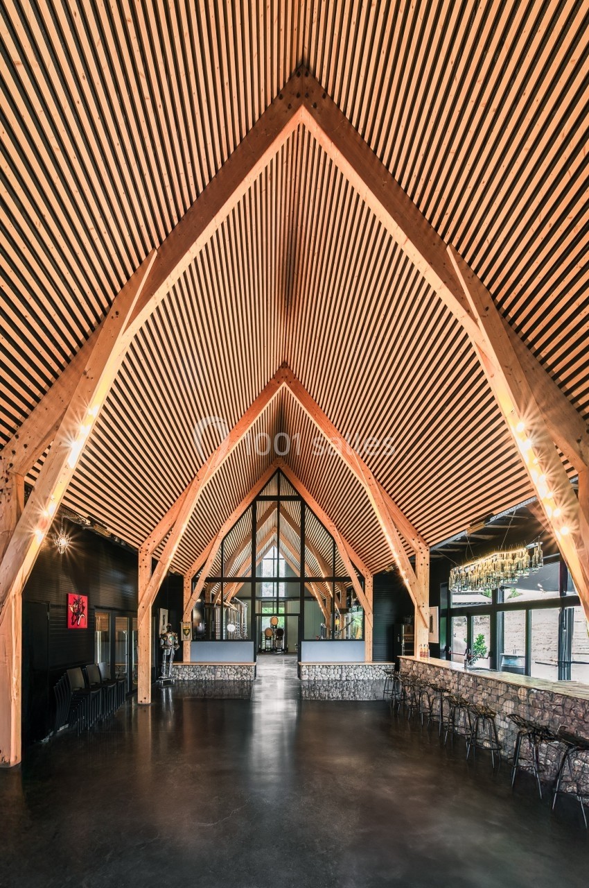 Intérieur d'une grande salle avec une charpente en bois apparente et un plafond à lattes, éclairée par des baies vitrées.