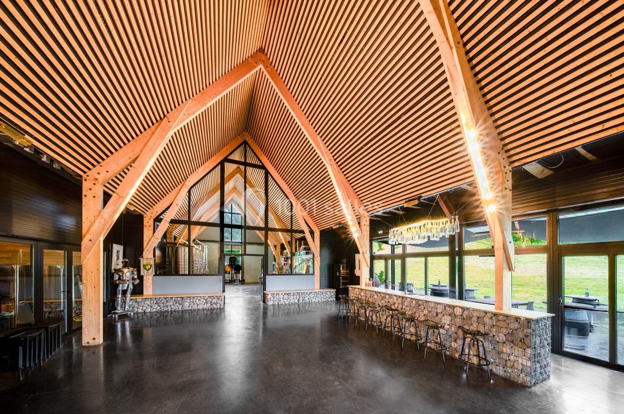 Intérieur d'un bâtiment moderne avec une charpente en bois apparente, des murs vitrés et un comptoir en pierre.