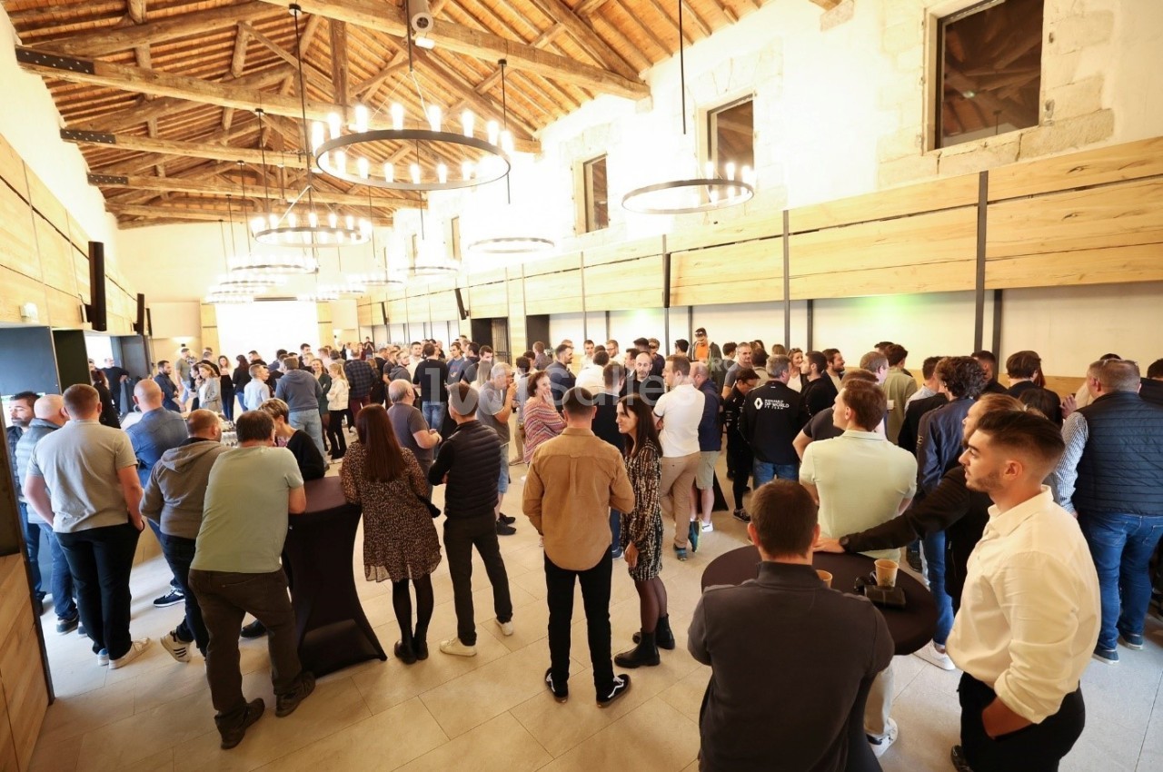 Groupe de personnes échangeant dans une grande salle lumineuse avec plafond en bois et lustres circulaires.