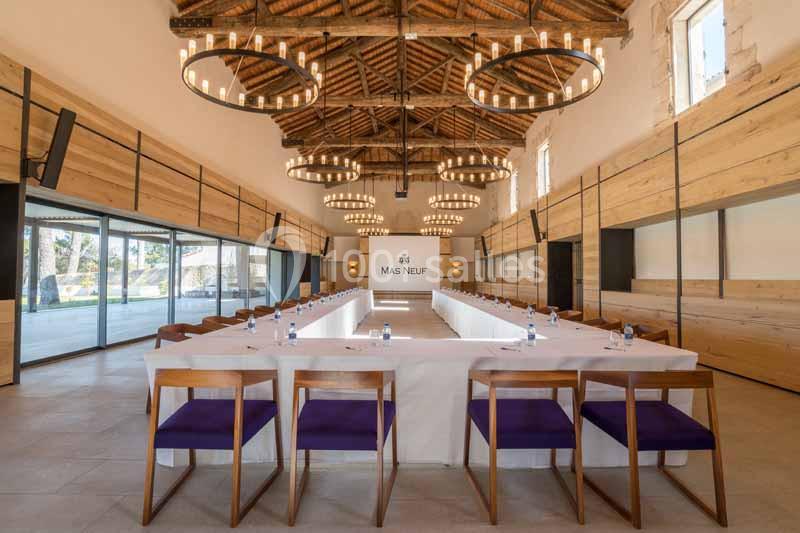 Salle de réunion lumineuse avec une grande table en U, chaises en bois, plafond en poutres apparentes et lustres suspendus.