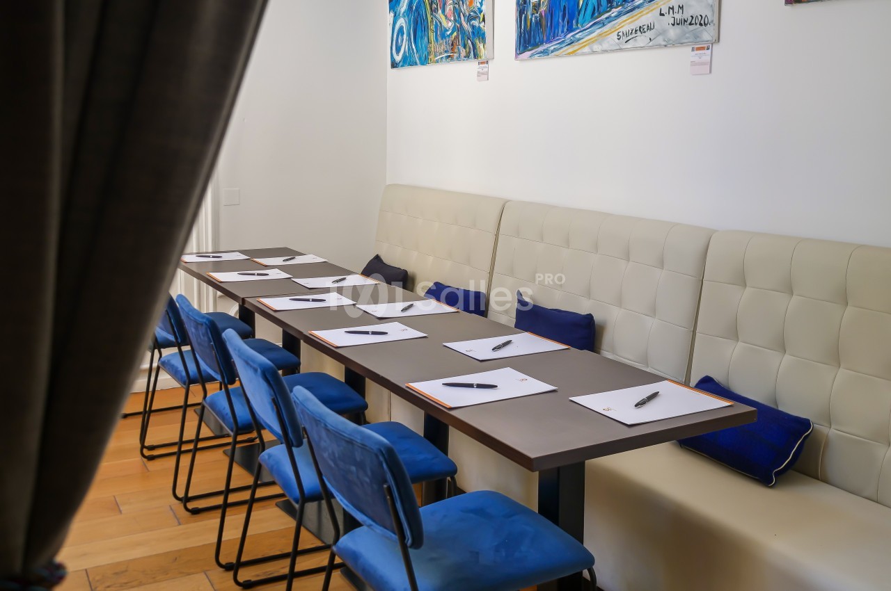 Salle de réunion avec une table rectangulaire, chaises bleues et carnets avec stylos alignés.