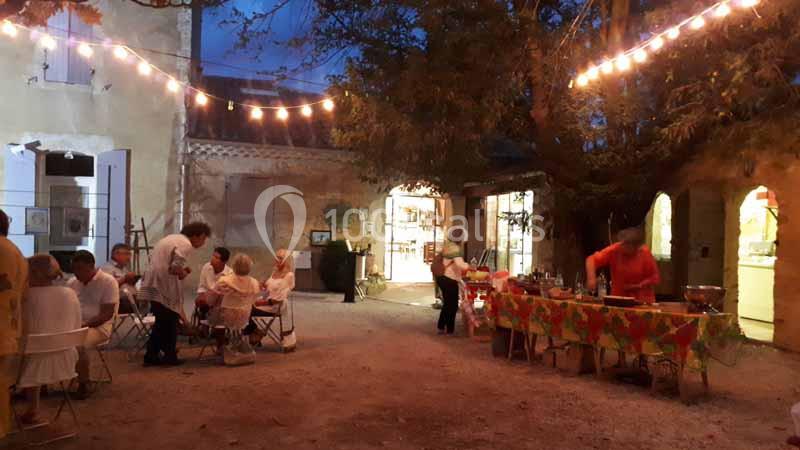 Location salle Caderousse (Vaucluse) - Domaine de la Lusignane #10 Cour extérieure éclairée par des guirlandes, avec des personnes dînant à des tables et un buffet en préparation.