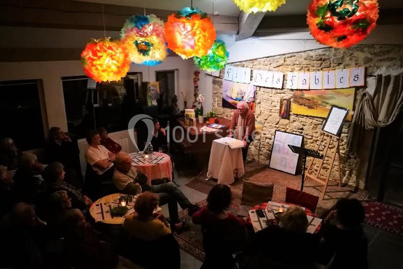 Location salle Caderousse (Vaucluse) - Domaine de la Lusignane #9 Un conteur s'adresse à un public assis dans une salle décorée de lampions colorés et d'affiches.