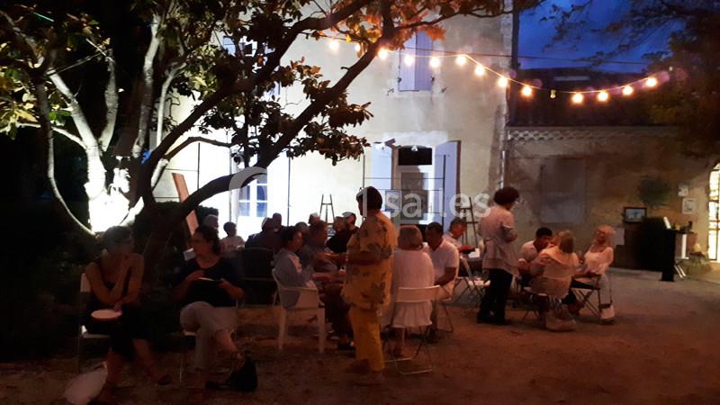 Location salle Caderousse (Vaucluse) - Domaine de la Lusignane #11 Groupe de personnes assises dans une cour éclairée par des guirlandes lumineuses, devant une maison en soirée.