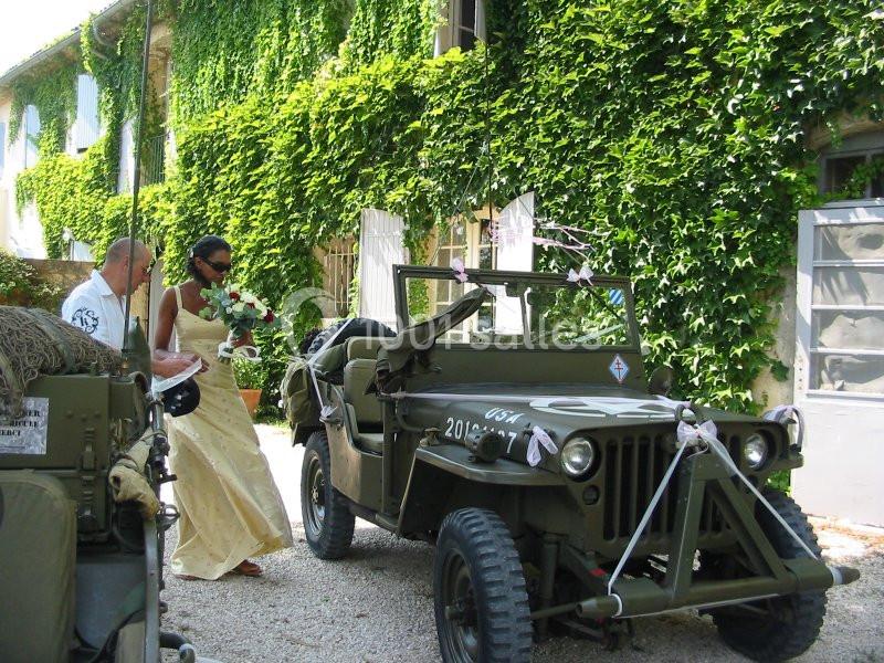 Location salle Caderousse (Vaucluse) - Domaine de la Lusignane #12 Une mariée monte dans une jeep militaire décorée, devant un bâtiment couvert de lierre.