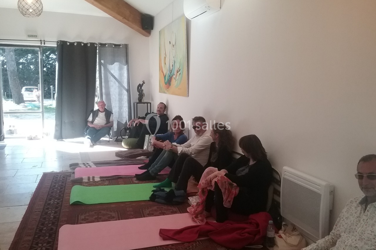 Location salle Caderousse (Vaucluse) - Domaine de la Lusignane #15 Des personnes assises sur des tapis et des chaises dans une salle lumineuse avec des œuvres d'art au mur.