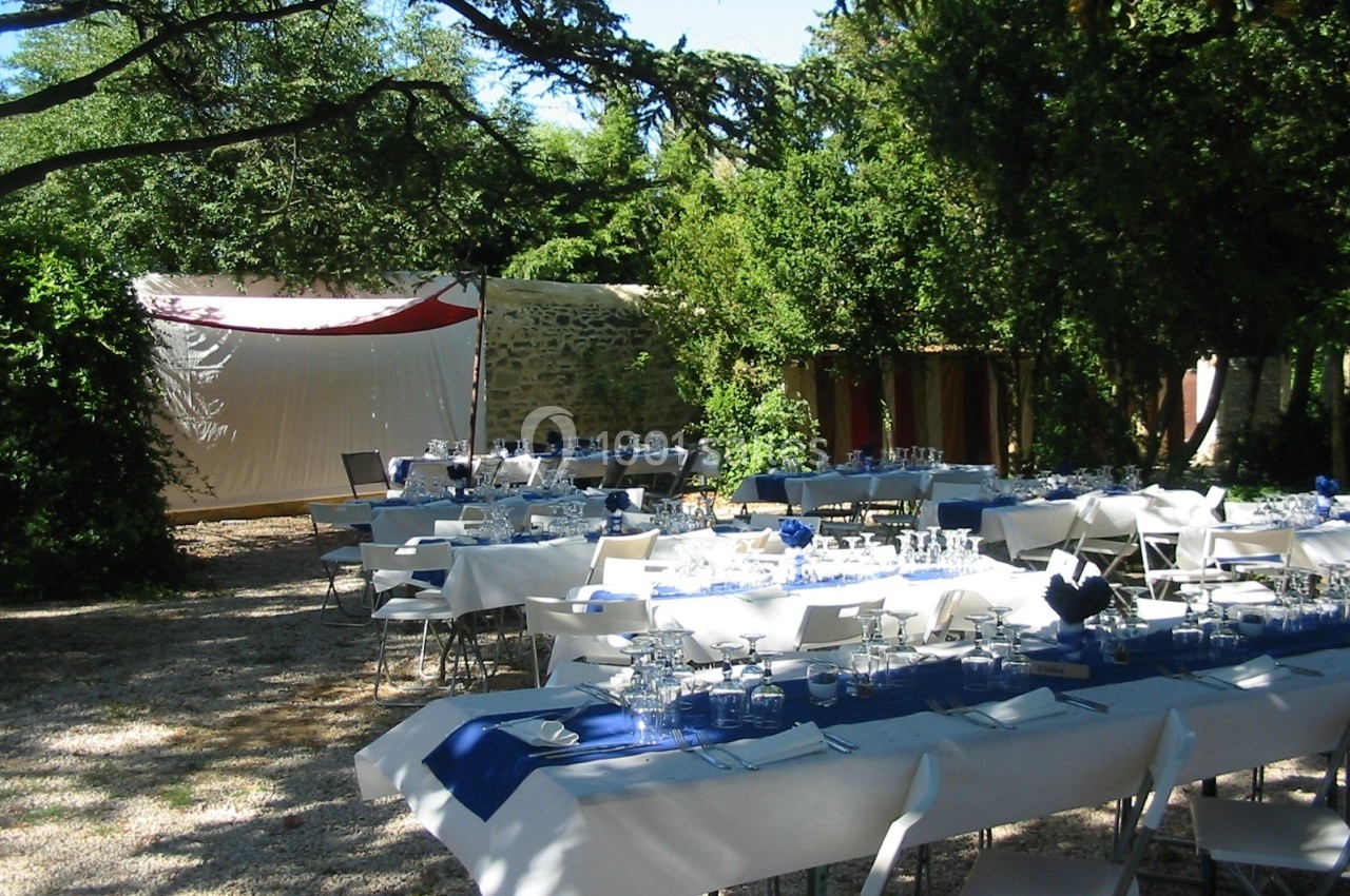 Location salle Caderousse (Vaucluse) - Domaine de la Lusignane #20 Tables dressées pour un repas en plein air sous des arbres, avec nappes blanches et décorations bleues.