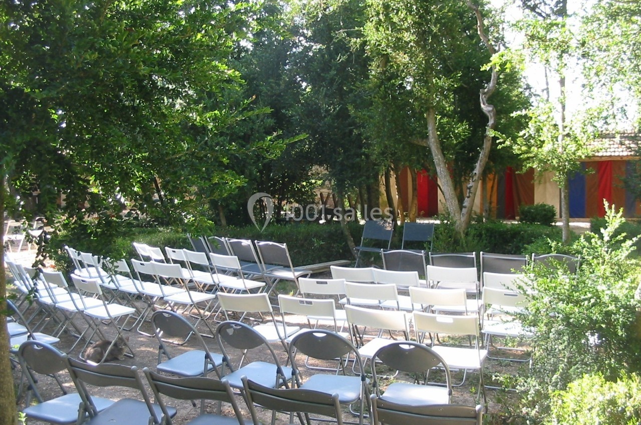 Location salle Caderousse (Vaucluse) - Domaine de la Lusignane #23 Chaises disposées en rangées dans un jardin ombragé, face à une structure colorée en arrière-plan.