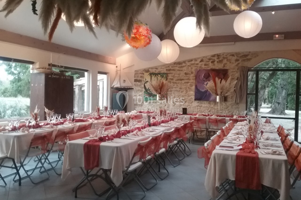 Location salle Caderousse (Vaucluse) - Domaine de la Lusignane #26 Salle décorée pour un événement, avec des tables alignées, nappes blanches, chemins de table rouges et lanternes suspendues.
