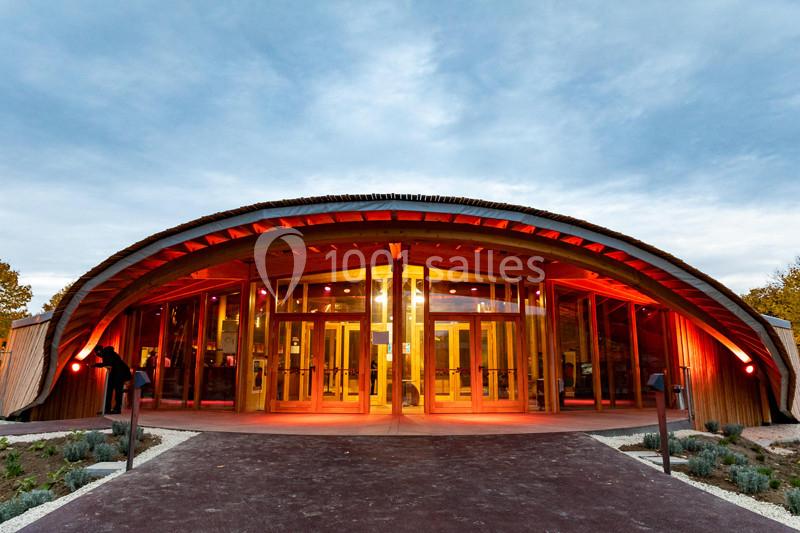 Entrée d'un bâtiment en bois avec une façade incurvée et des éclairages rouges sous un ciel nuageux.