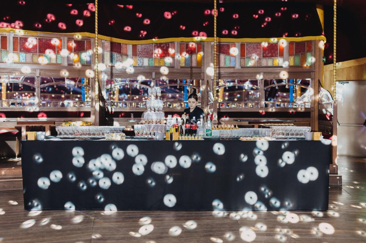 Un bar élégant avec boissons et verres alignés, éclairé par des lumières colorées dans une salle festive.