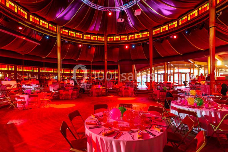 Salle circulaire décorée pour un événement, avec tables dressées, chaises pliantes et éclairage rouge et jaune.