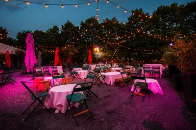 Terrasse extérieure avec tables rondes, chaises pliantes et guirlandes lumineuses suspendues, ambiance en soirée.
