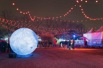 Terrasse extérieure avec tables rondes, chaises pliantes et guirlandes lumineuses suspendues, ambiance en soirée.