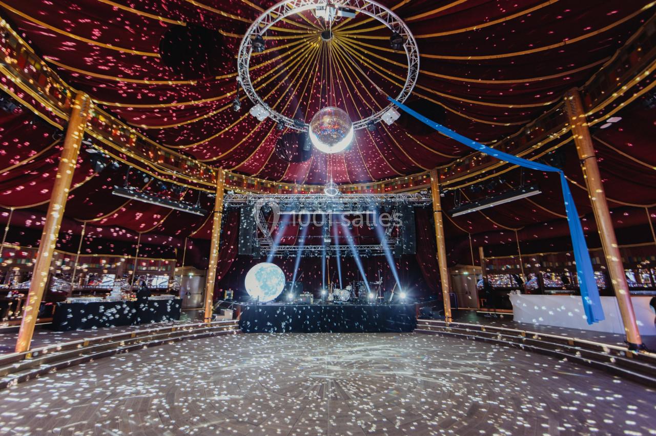 Intérieur d'un chapiteau avec piste de danse, éclairages colorés et boule à facettes suspendue au plafond.
