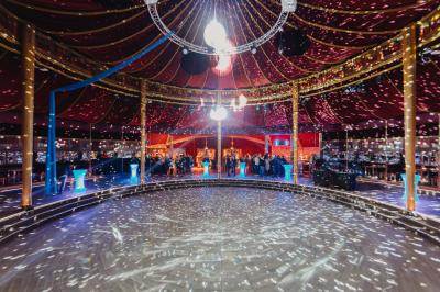 Terrasse extérieure avec tables rondes, chaises pliantes et guirlandes lumineuses suspendues, ambiance en soirée.