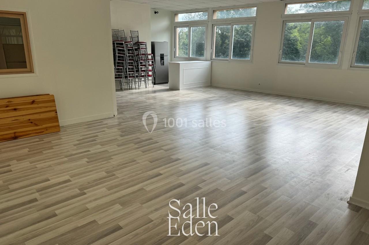 Salle lumineuse avec parquet clair, grandes fenêtres, chaises empilées au fond et un comptoir blanc.