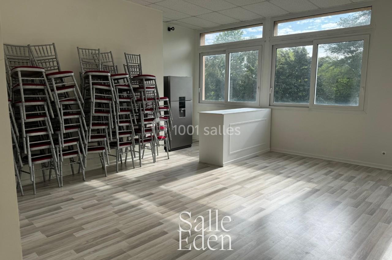 Salle lumineuse avec parquet clair, chaises empilées sur la gauche, comptoir blanc et grandes fenêtres donnant sur des…