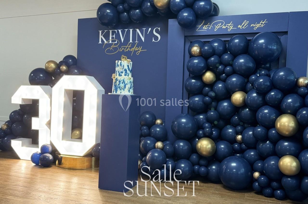 Décoration d'anniversaire avec ballons bleu marine et dorés, chiffre lumineux ’30’ et gâteau sur un présentoir.