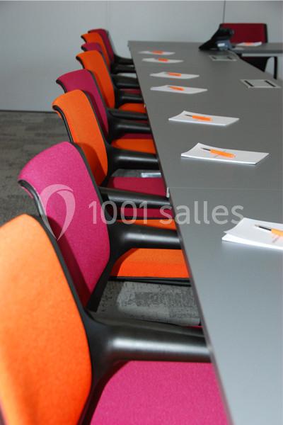 Location salle Louveciennes (Yvelines) - Campus BNP Paribas Louveciennes #22 Chaises colorées alignées le long d'une table grise avec des carnets et stylos orange posés devant chaque siège.
