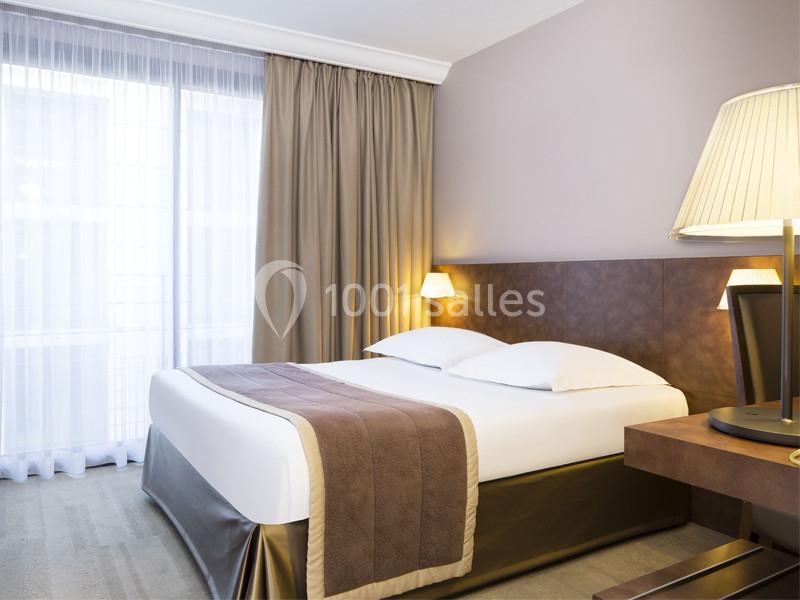 Location salle Louveciennes (Yvelines) - Campus BNP Paribas Louveciennes #21 Chambre d'hôtel lumineuse avec un lit double, des draps blancs, des rideaux beiges et une lampe de chevet allumée.