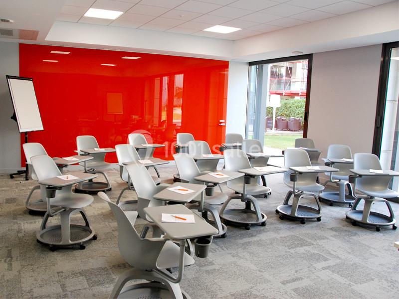 Location salle Louveciennes (Yvelines) - Campus BNP Paribas Louveciennes #5 Salle de classe moderne avec des chaises équipées de tablettes, un mur rouge vif et un tableau de conférence.