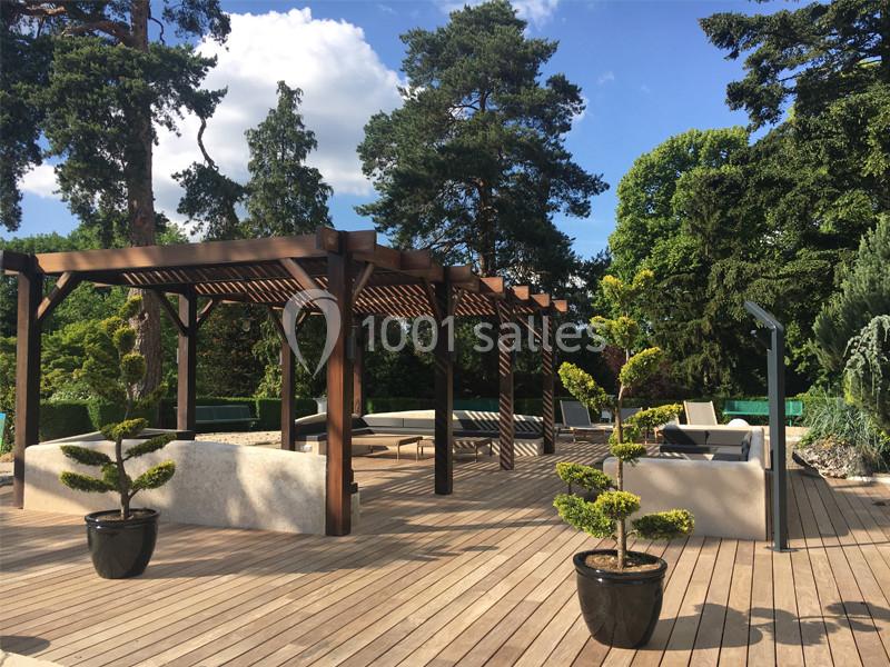 Location salle Louveciennes (Yvelines) - Campus BNP Paribas Louveciennes #17 Terrasse en bois avec pergola en bois sombre, mobilier de jardin et plantes en pots, entourée de végétation dense.