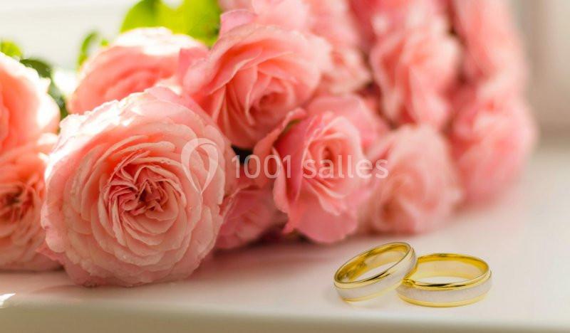 Bouquet de roses roses posé sur une surface blanche avec deux alliances dorées au premier plan.
