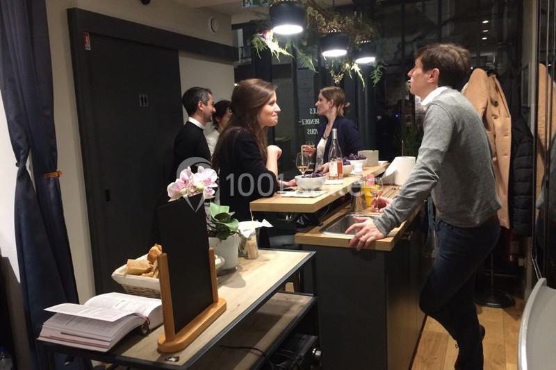 Location salle Paris 11 (Paris) - Les Rendez-vous #6 Des personnes discutent autour d'un comptoir dans un espace intérieur moderne et éclairé, avec des plantes suspendues.
