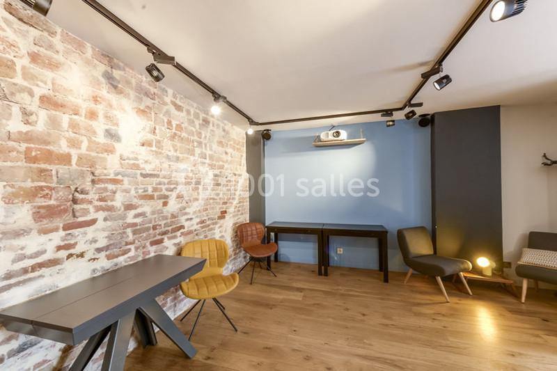 Location salle Paris 11 (Paris) - Les Rendez-vous #1 Salle lumineuse avec mur en briques, parquet, mobilier moderne et projecteur fixé au plafond.