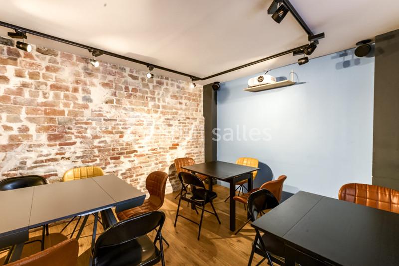 Location salle Paris 11 (Paris) - Les Rendez-vous #11 Salle lumineuse avec murs en briques et peinture bleue, tables noires, chaises variées et projecteur au plafond.