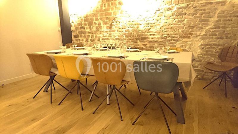 Location salle Paris 11 (Paris) - Les Rendez-vous #7 Table dressée avec vaisselle et verres, entourée de chaises colorées dans une pièce avec mur en briques apparentes.