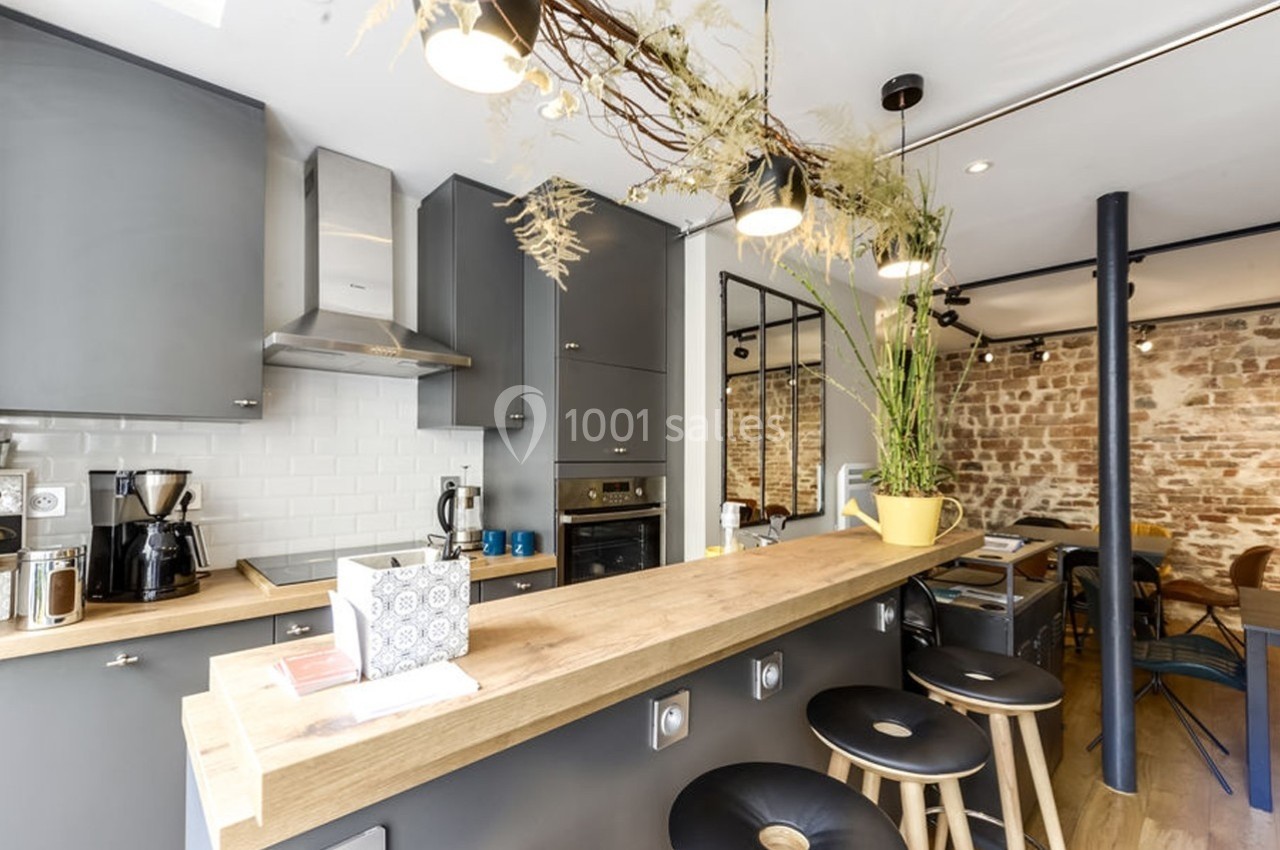 Location salle Paris 11 (Paris) - Les Rendez-vous #1 Cuisine moderne avec comptoir en bois, tabourets noirs, murs en briques apparentes et éclairage suspendu.