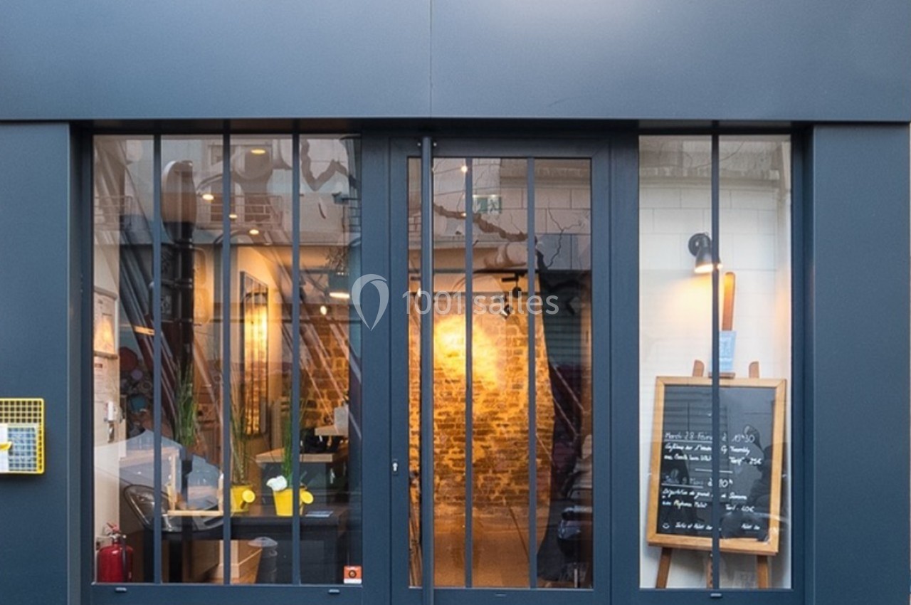Location salle Paris 11 (Paris) - Les Rendez-vous #12 Façade d'un restaurant avec une porte vitrée, un tableau noir affichant le menu et un intérieur éclairé visible.